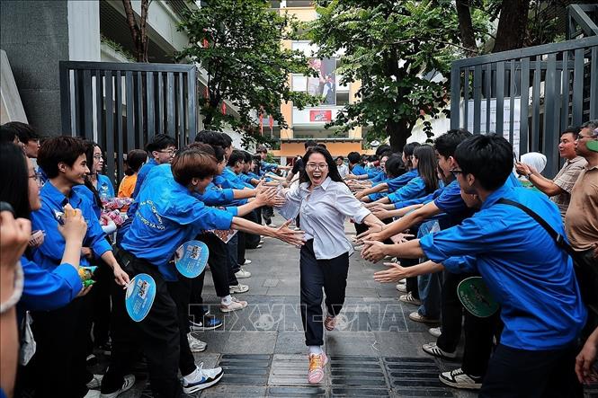 Tình nguyện viên xếp thành hai hàng, vỗ tay chào đón thí sinh đầu tiên rời khỏi điểm thi Trường THCS Ngô Sĩ Liên sau khi kết thúc môn thi đầu tiên. Ảnh: Phạm Tuấn Anh - TTXVN
